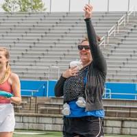 Woman holding a baby to her chest while throwing a cornhole bag